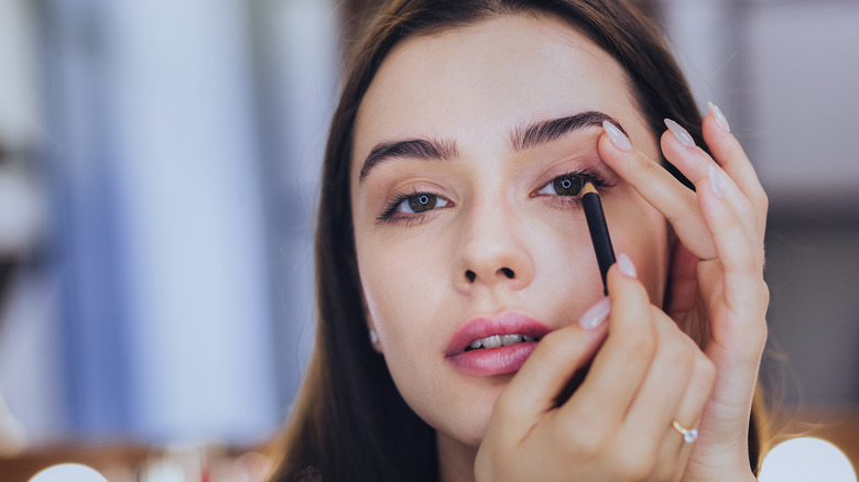Woman applies pencil eyeliner 