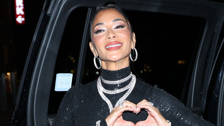 Nicole Scherzinger posing with a heart sign and lots of makeup