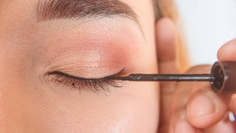 Applying eyeliner to woman's eyes