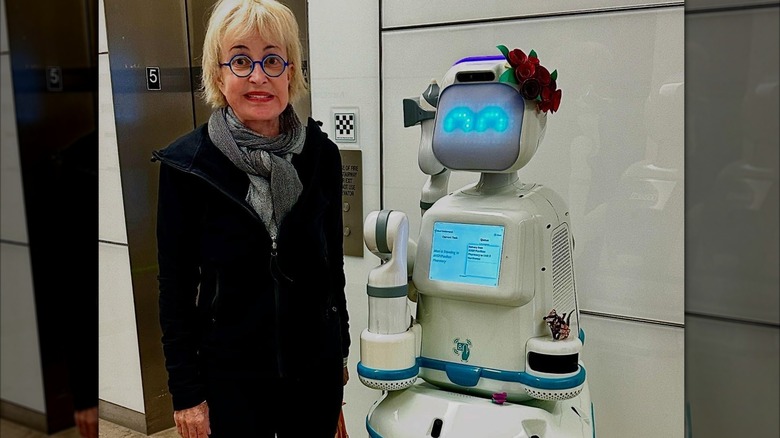 Annie Potts with a robot in a hospital as she wears minimal makeup