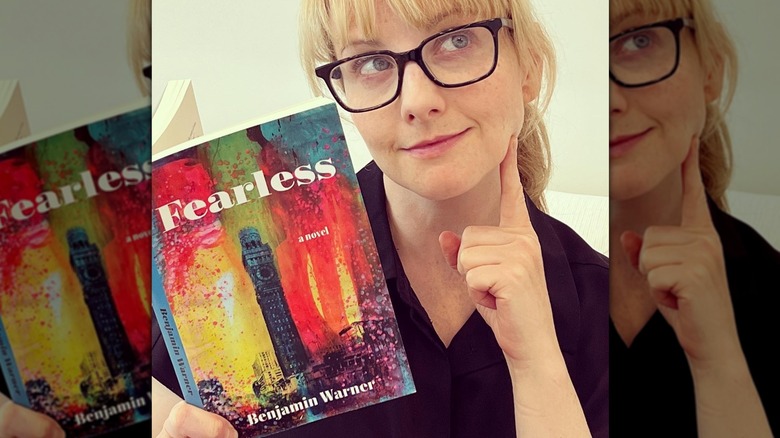 Melissa Rauch wearing glasses with little makeup as she poseswith book
