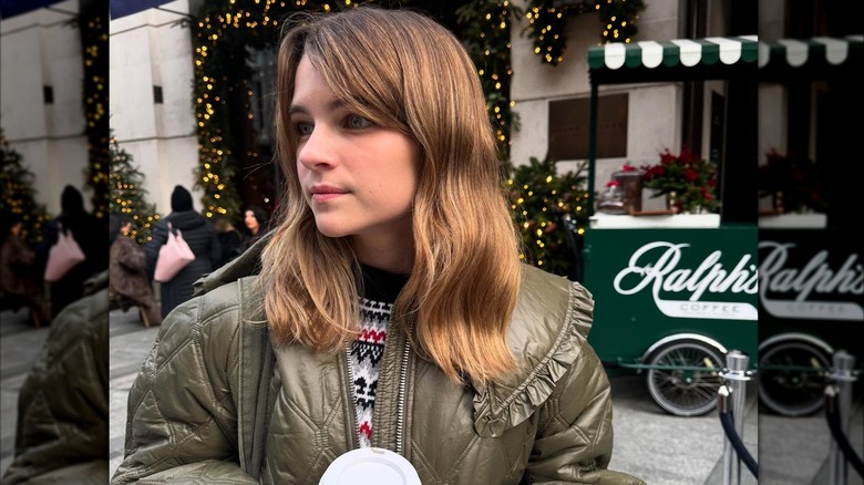 Raegan Revord holding drink in front of Christmas lights while wearing minimal makeup