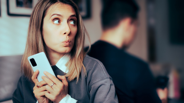 woman holding phone and looking sneaky