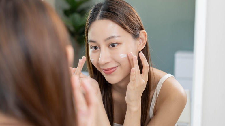 Woman applies foundation in mirror 