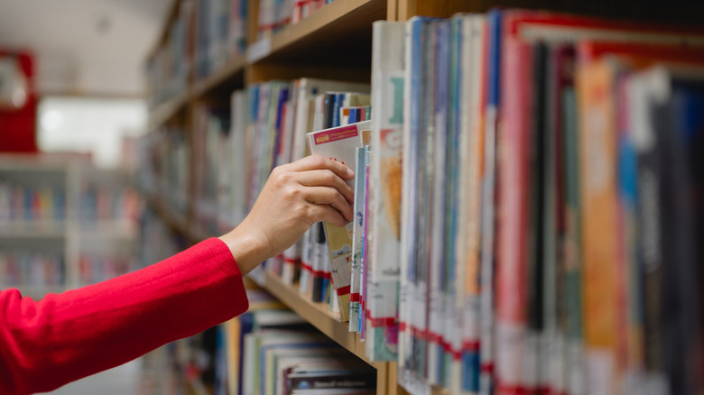 A hand reaching for a book in a library