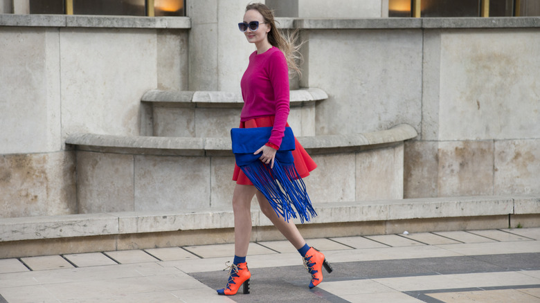 A woman wearing a pink Benetton sweater with her red skirt and blue purse