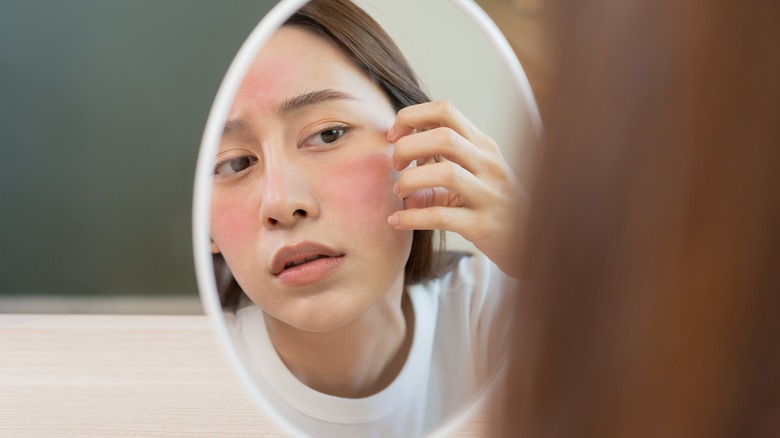 Woman with red skin looking in mirror