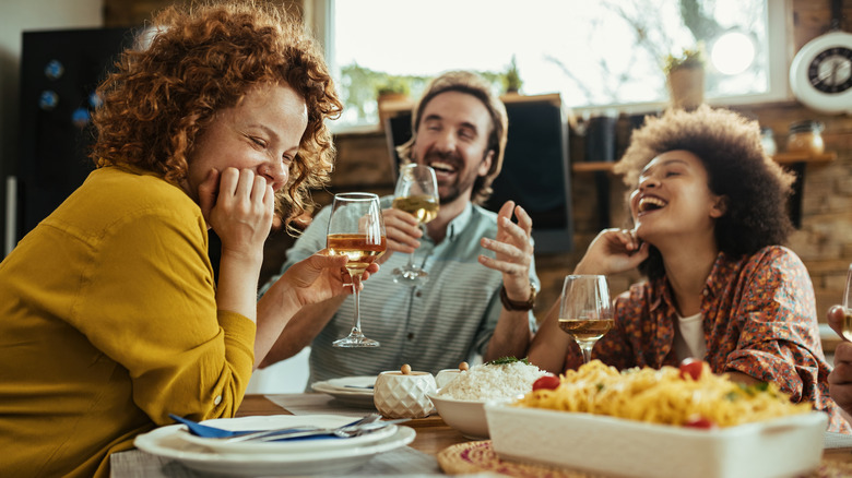 Three people laughing over wine