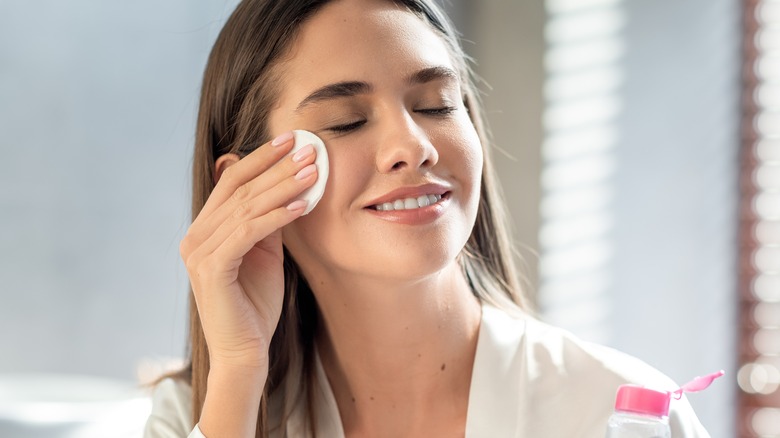 woman applying micellar water on face with cotton pad