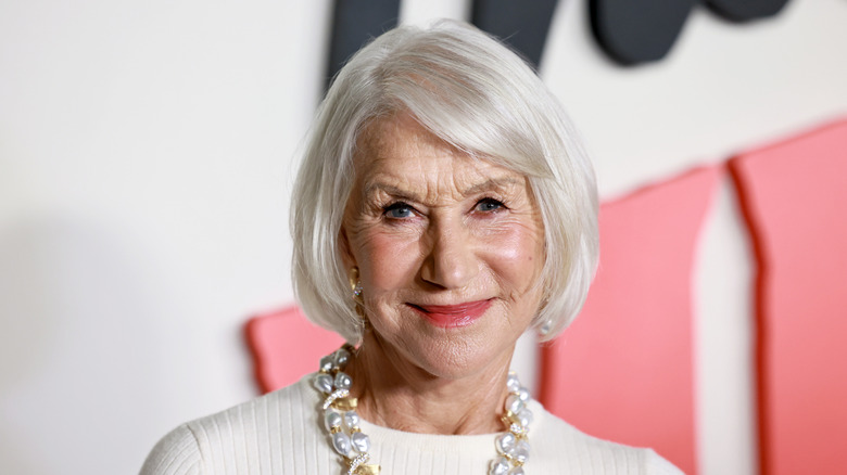 Helen Mirren smiling on a white top with an elegant necklace