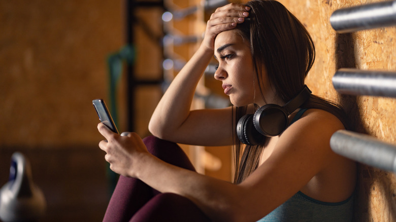 Woman sits scrolling through phone in home gym