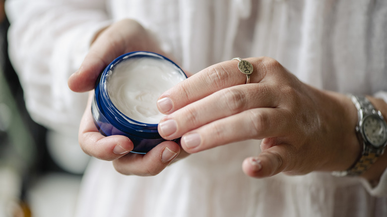 Person with natural nails holding a tub of cream