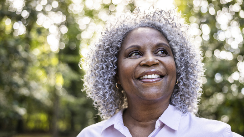An older woman with a curly gray lob smiles widely while posing for a photo