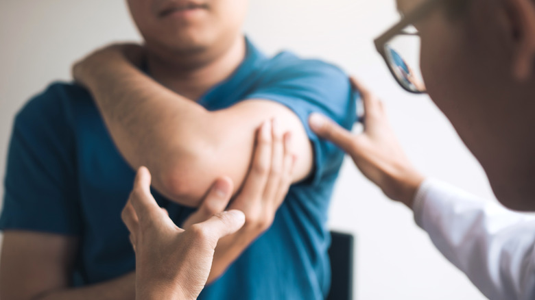 doctor examining arm of male patient