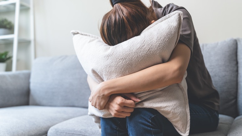 stressed woman sitting on couch with head in pillow