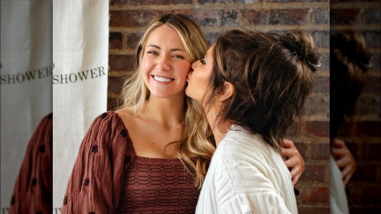 Kristi Noem kisses daughter Kennedy on the cheek in front of a brick wall at her baby shower