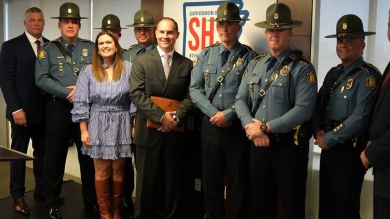 Sarah Huckabee Sanders smiling in a blue-and-white dress with brown boots while posing with police officers